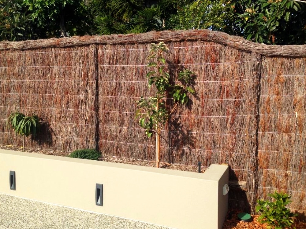 A brushwood fence that has been well-maintained with small shrubs in front